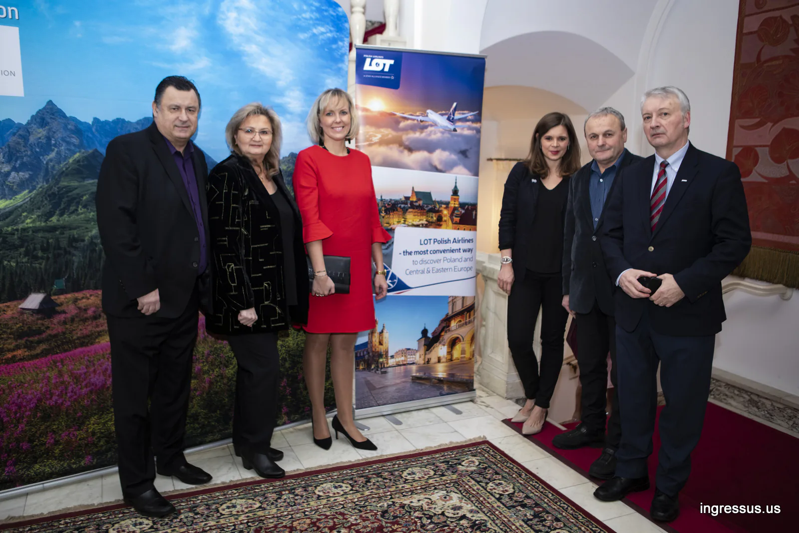 Six guests posing by a LOT Polish Airlines roll-up banner and a mountain backdrop at the Polish Consulate General in Chicago
