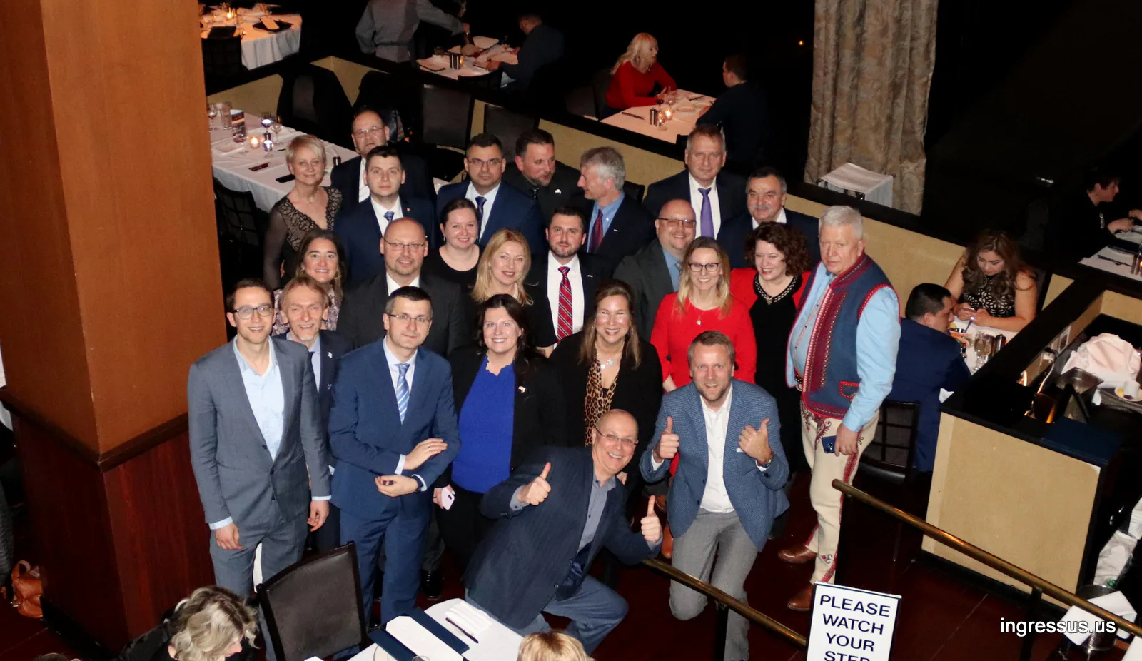 Large group of guests posing in a restaurant, several giving a thumbs up, one man wearing a highlander vest