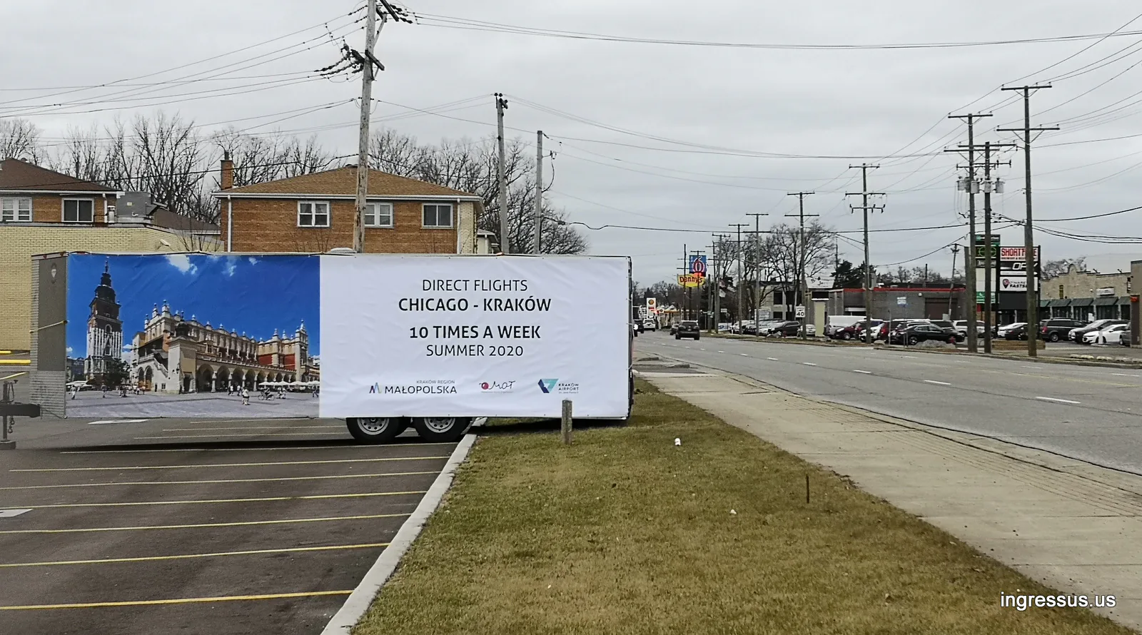 Roadside banner trailer with a Kraków Main Market Square photo advertising direct flights Chicago to Kraków 10 times a week in summer 2020