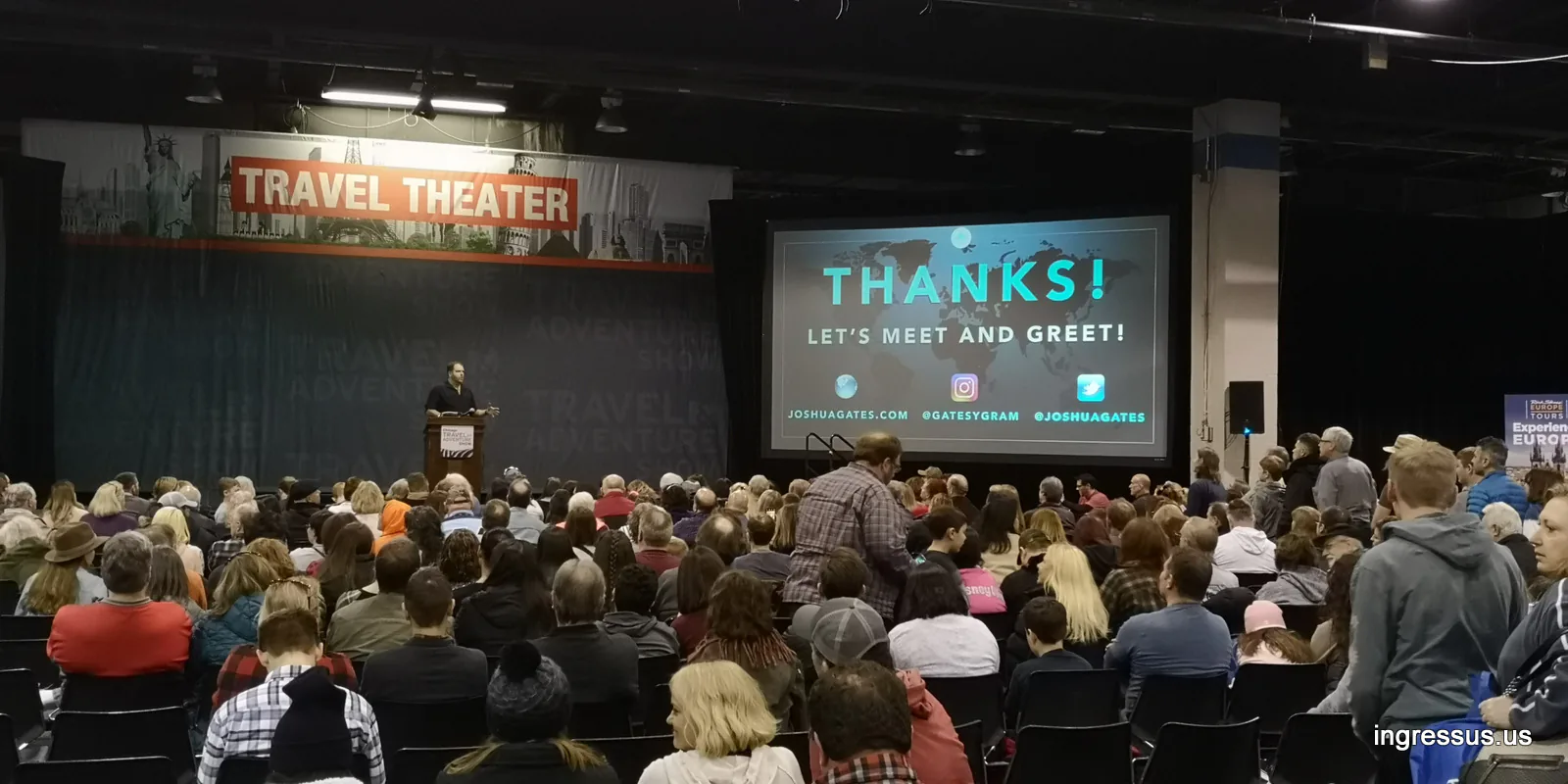 Packed Travel Theater at the 2020 Travel & Adventure Show, with a speaker at the podium and a Thanks! Let's meet and greet! slide