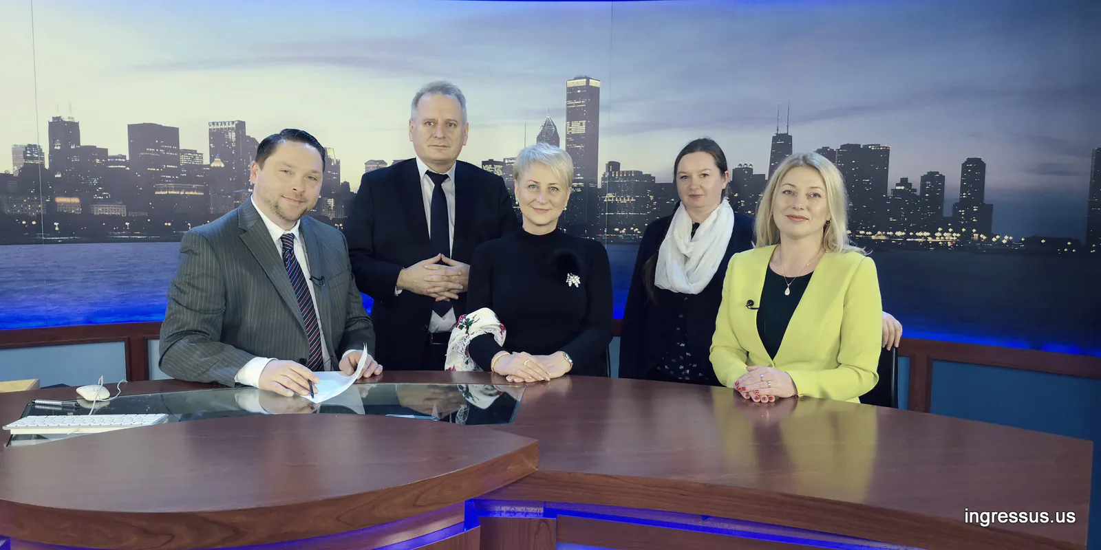 Five people at a TV studio news desk with a Chicago skyline backdrop after a promotional television interview