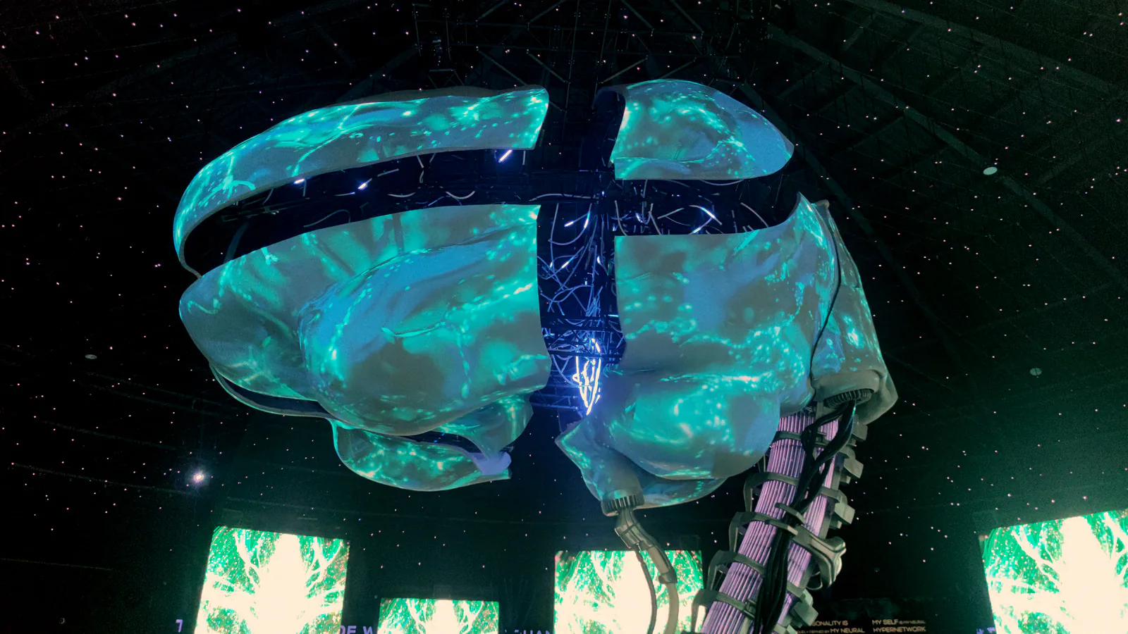 Giant brain sculpture lit with blue and green projections under a starry dome inside a pavilion at Expo 2020 Dubai