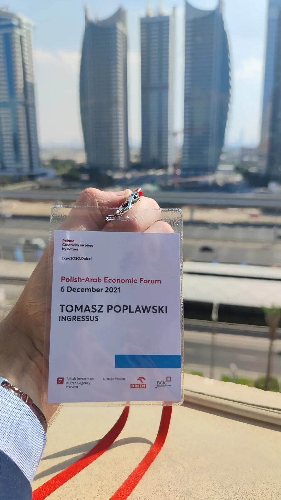 Tomasz Popławski's Ingressus badge for the Polish-Arab Economic Forum, 6 December 2021, held up against Dubai towers