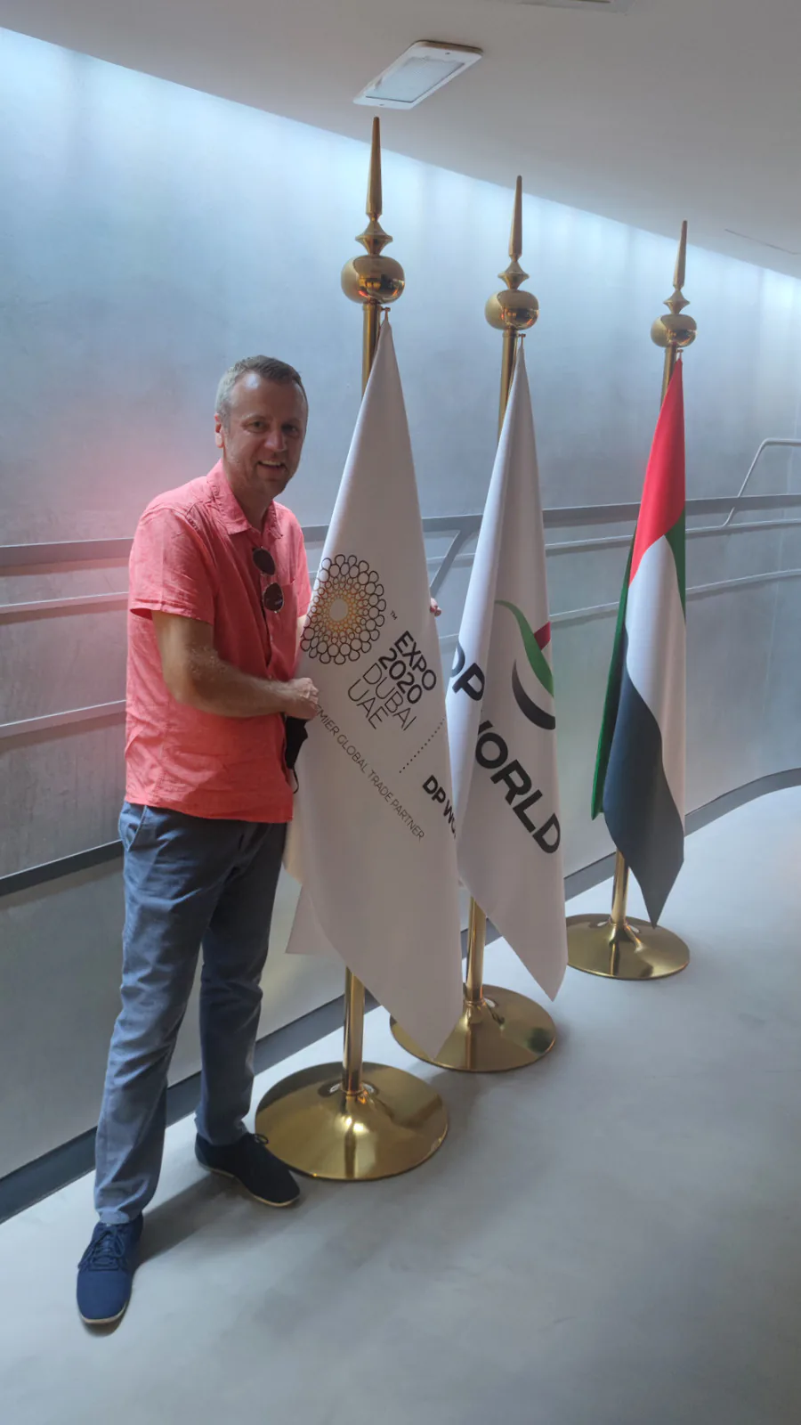 Trade mission participant beside an Expo 2020 Dubai flag, a DP World flag and the flag of the United Arab Emirates
