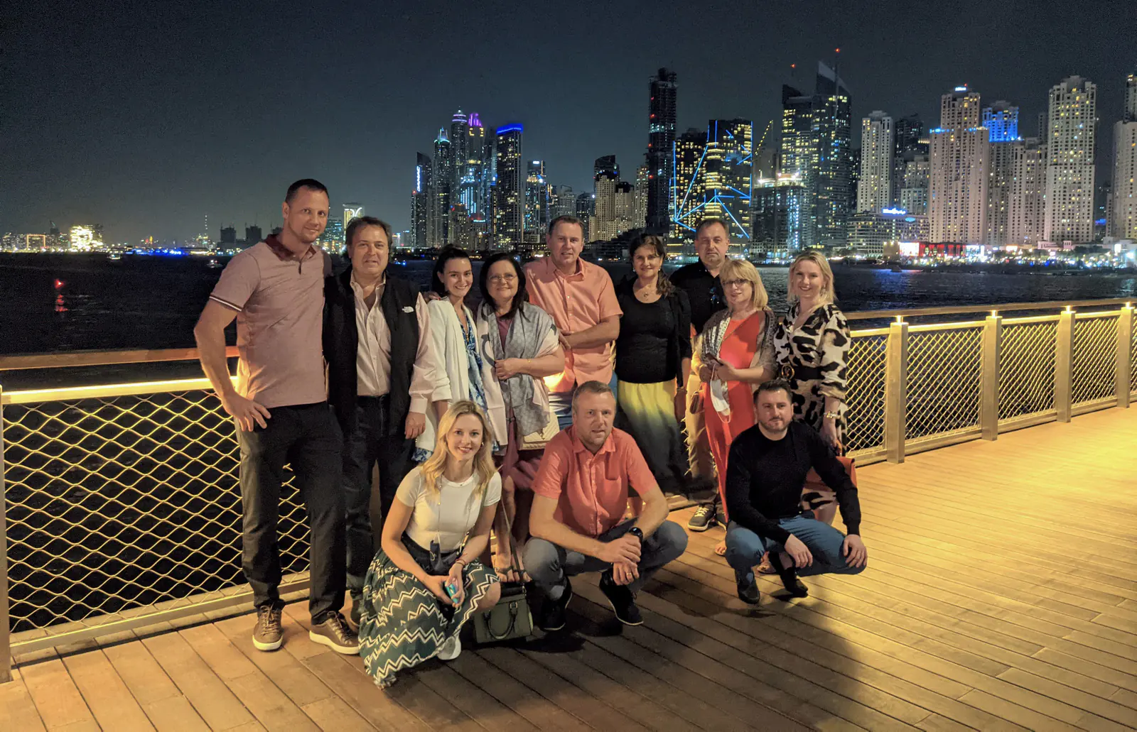Trade mission participants posing on a waterfront boardwalk at night with the lit Dubai Marina skyline behind