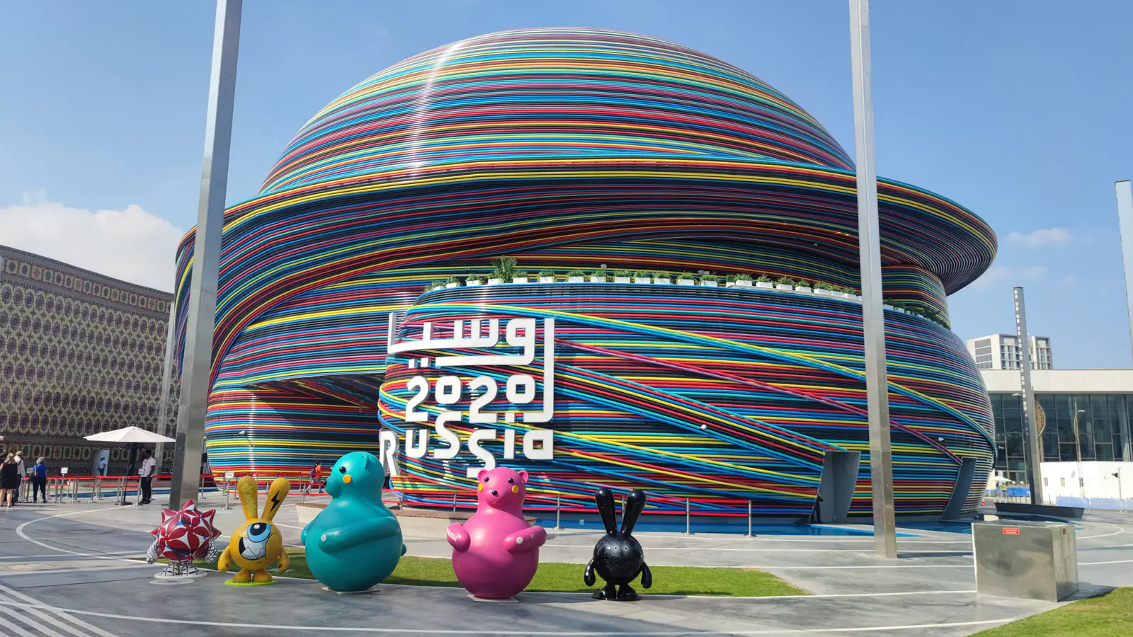 Russia pavilion at Expo 2020 Dubai wrapped in colorful stripes, with large cartoon animal figures in front
