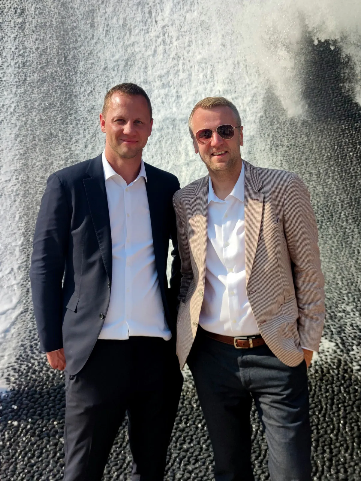 Two trade mission participants in blazers posing in front of a water wall at Expo 2020 Dubai