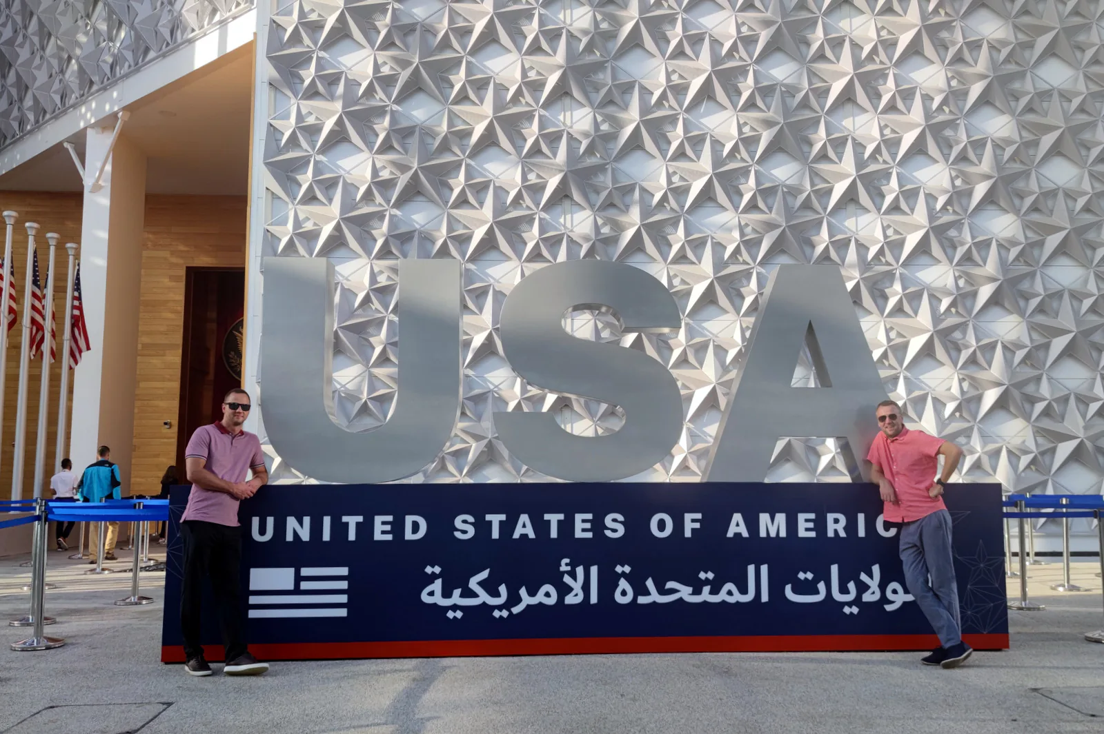 Two trade mission participants at the large USA sign in front of the United States of America pavilion at Expo 2020 Dubai