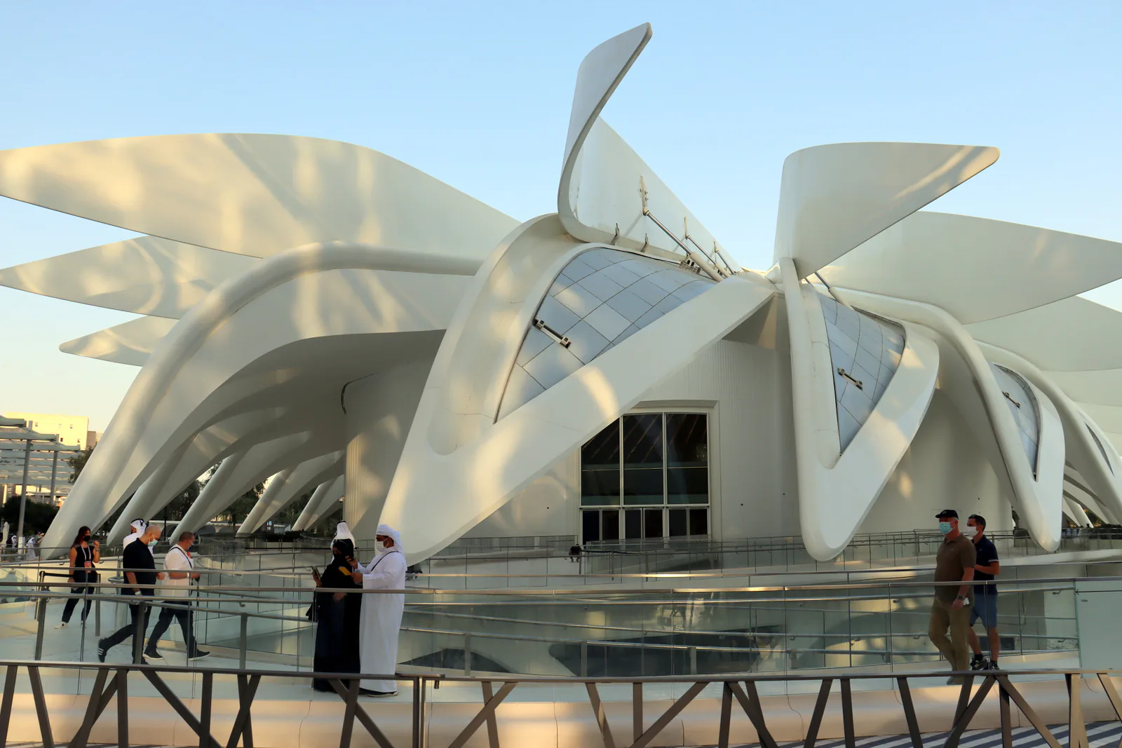 Visitors walking past a white pavilion with sweeping wing-like roof panels at Expo 2020 Dubai