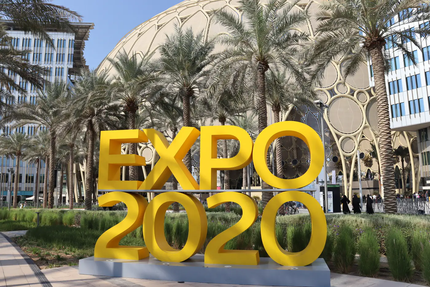 Yellow EXPO 2020 letters among palm trees, with the Al Wasl Plaza dome rising behind them in Dubai
