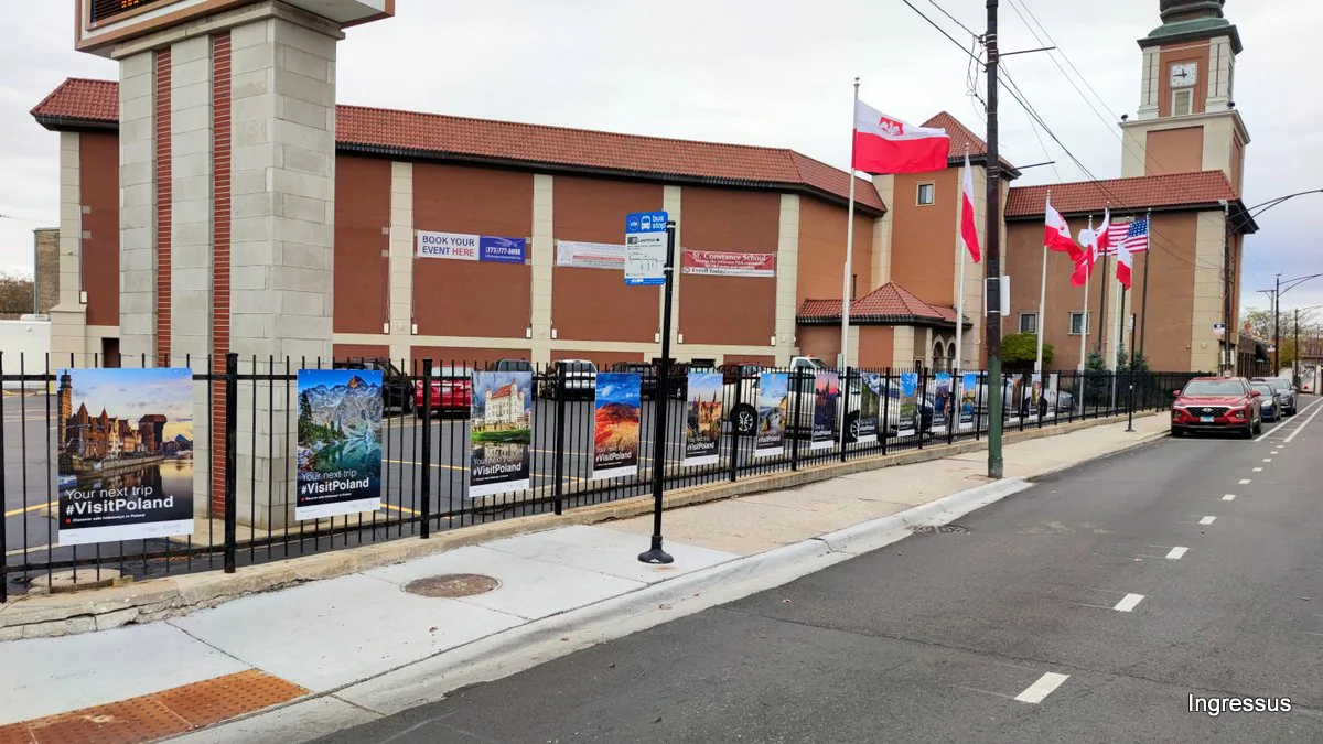 Wide view of the #VisitPoland exhibition along the Copernicus Foundation fence in Chicago, with Polish and U.S. flags and the clock tower
