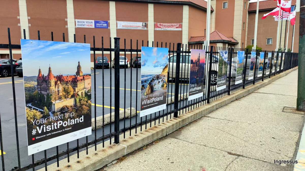 Row of #VisitPoland posters, starting with Książ Castle, stretching along the Copernicus Foundation fence toward the flagpoles