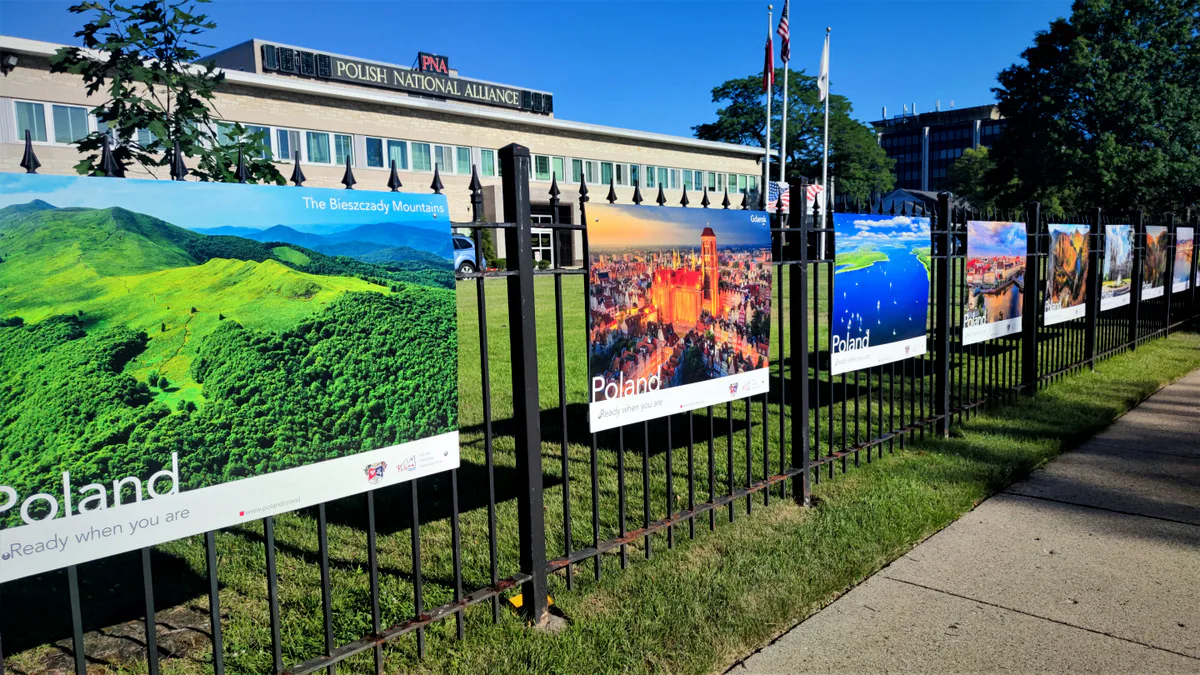 Bieszczady Mountains and Gdańsk posters leading a row of Polish travel posters on the fence along the sidewalk at the PNA