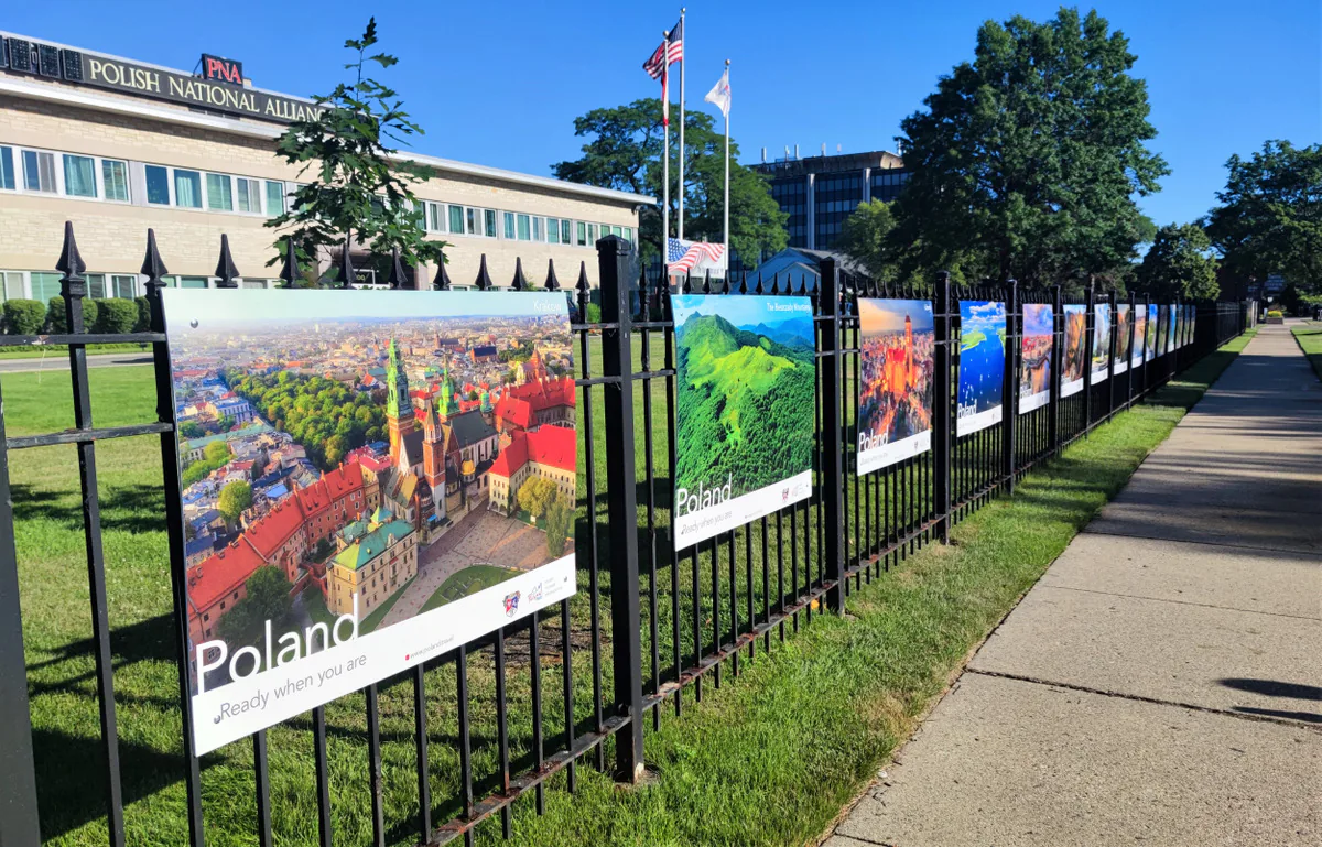Aerial Kraków poster at the start of a long row of Poland travel posters on the fence beside the sidewalk at the PNA in Chicago