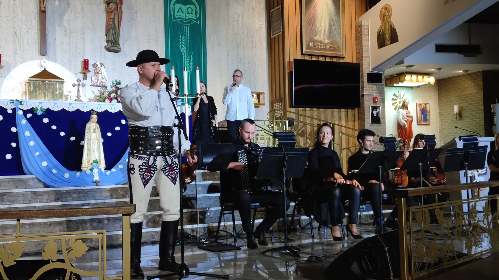 Singer in a Polish highlander folk costume performing with accordion and string players during The Saint concert
