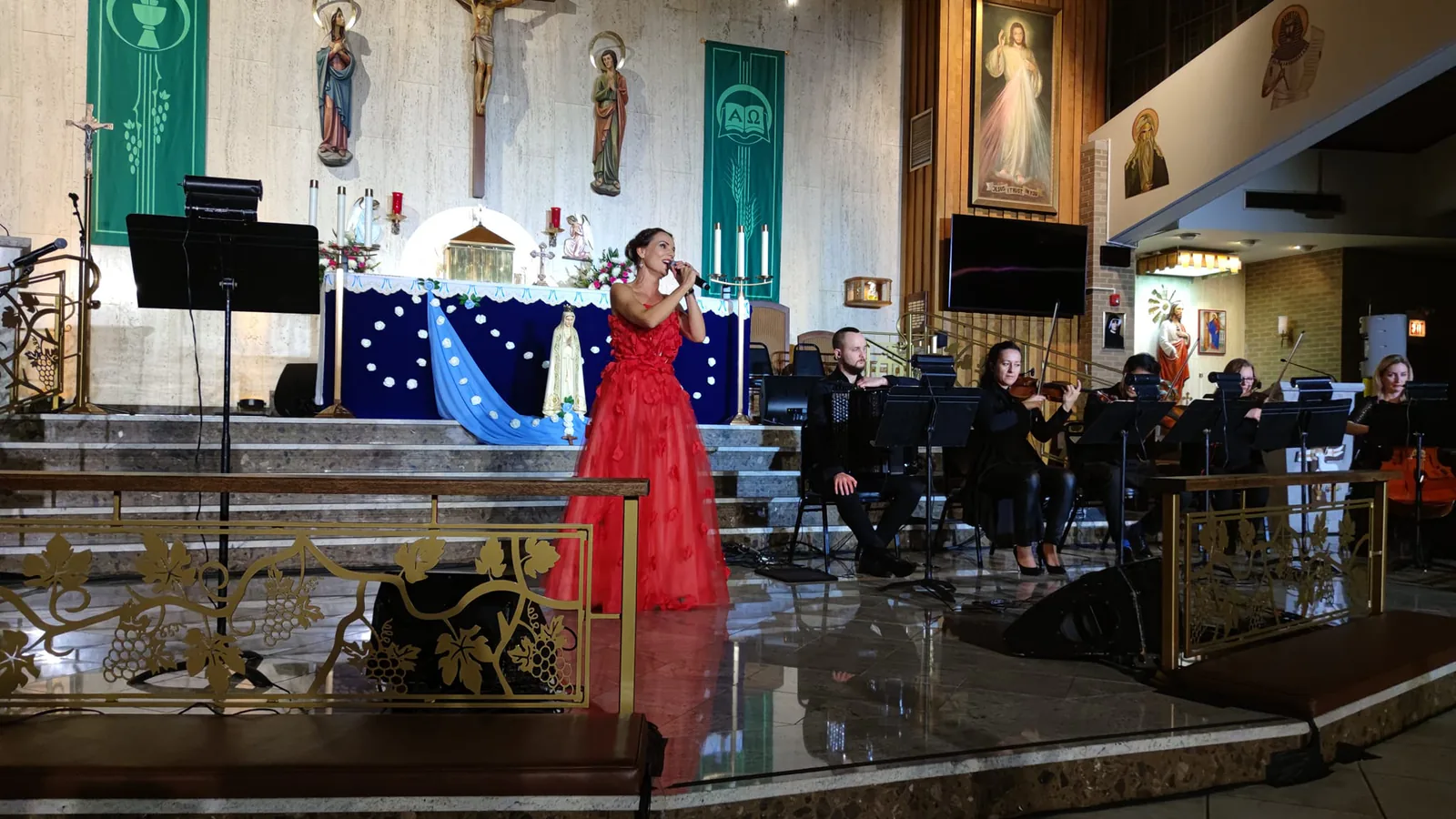 Singer in a red gown performing with a chamber ensemble in front of the altar during The Saint concert for John Paul II