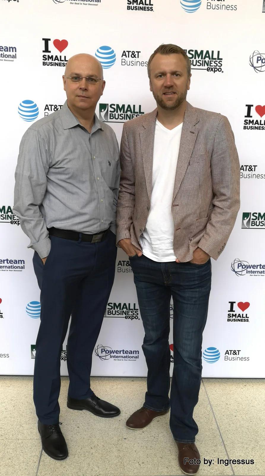 Two attendees posing in front of the Small Business Expo sponsor wall with AT&T Business and Powerteam International logos, 2019