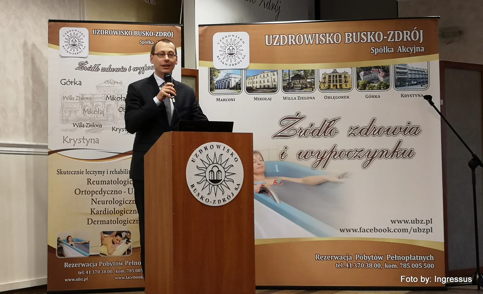 Speaker at the Uzdrowisko Busko-Zdrój podium in front of banners showing the spa's sanatoriums, 2019 study tour