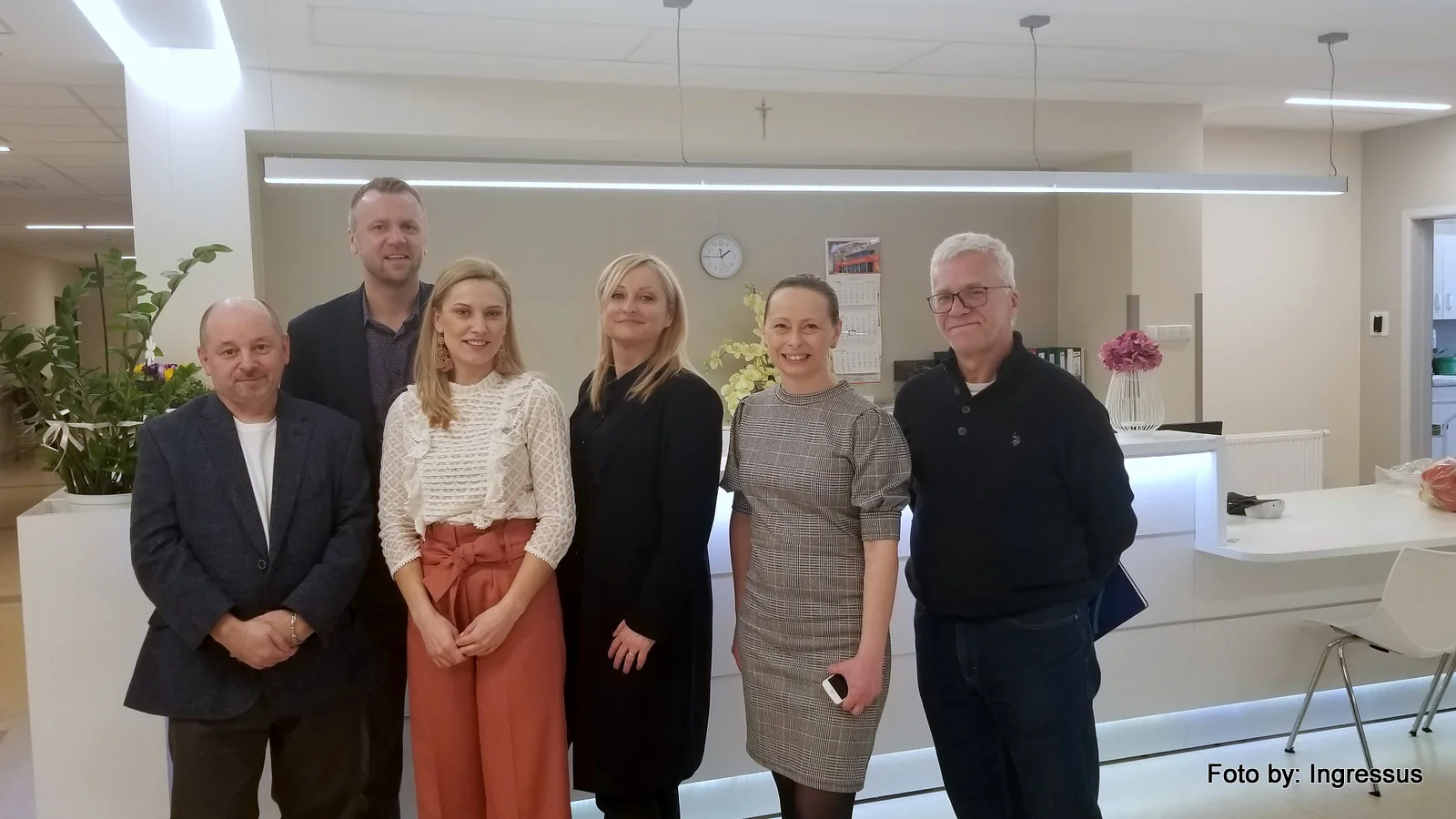Six members of the study tour posing at the bright reception desk of a Polish medical facility, March 2019