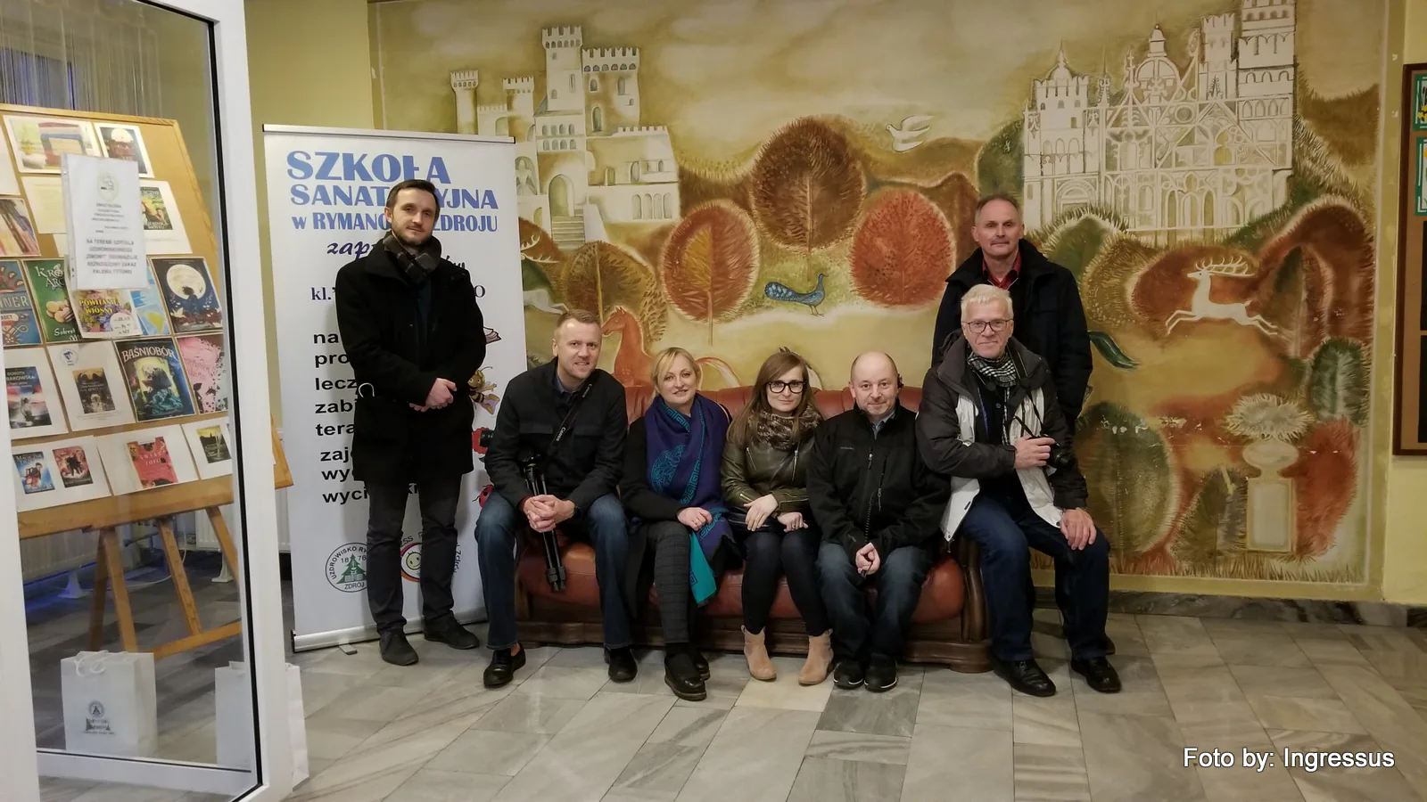 Study tour group on a sofa in front of a castle mural, next to a Szkoła Sanatoryjna w Rymanowie-Zdroju banner