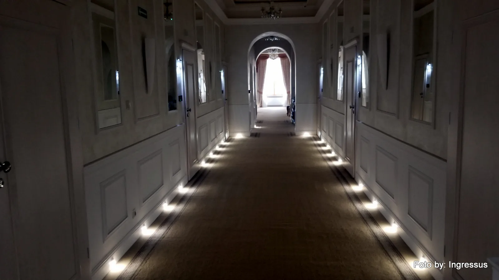 Elegant spa hotel corridor with paneled walls and floor-level lights leading to a curtained window