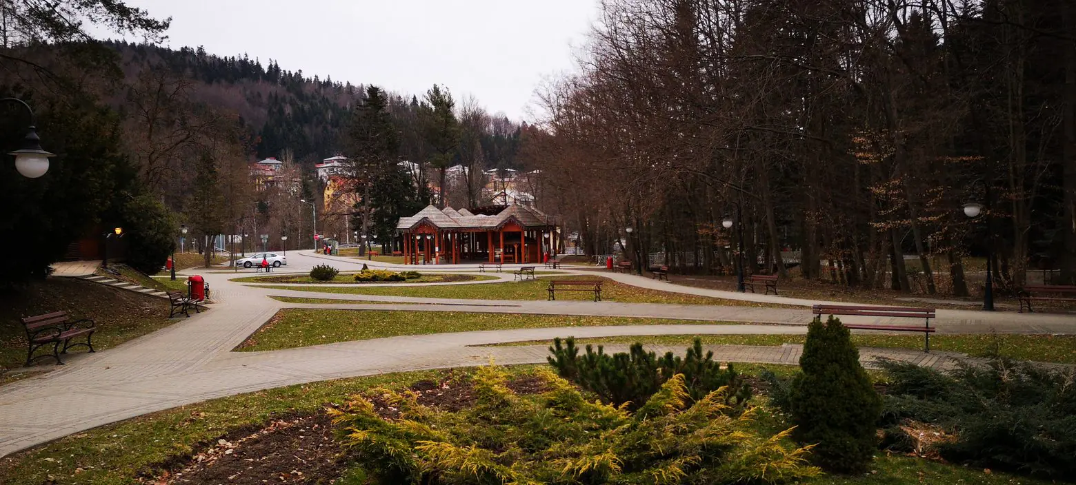 Spa park with winding paths, benches and a wooden pavilion below forested hills, seen during the 2019 study tour