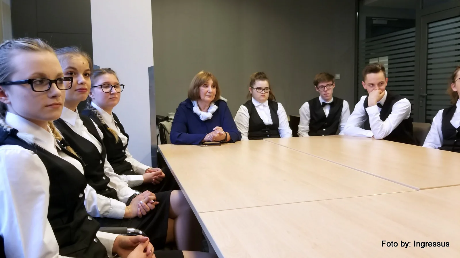 Students in white shirts and black waistcoats meeting the study tour with a teacher at a conference table