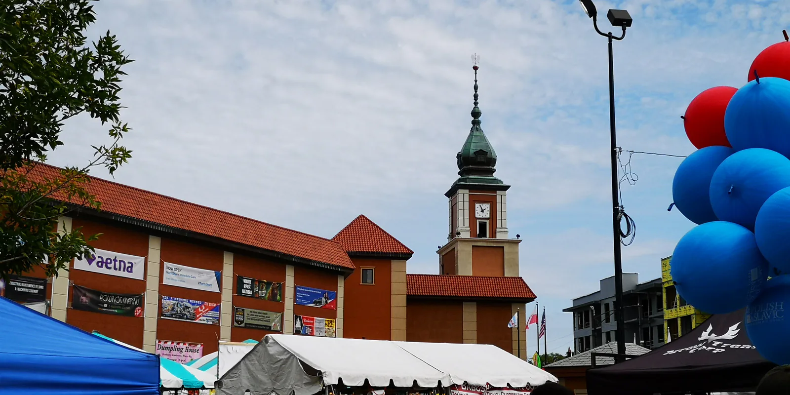 Copernicus Center clock tower in Chicago above festival tents, sponsor banners and blue and red balloons during Taste of Polonia 2019