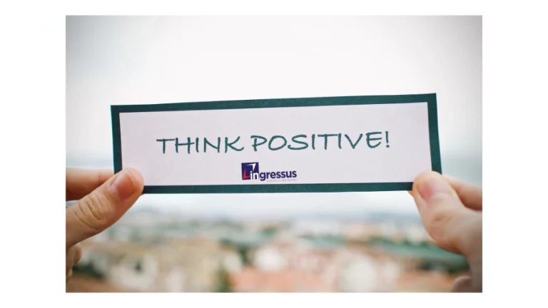 Hands holding a card with the words Think Positive and the Ingressus logo, against a blurred city background