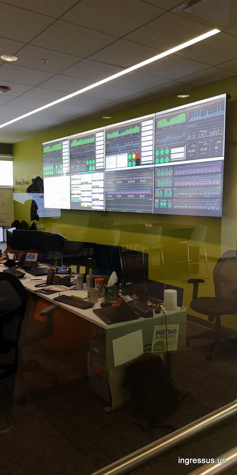 IT department at United Wholesale Mortgage seen through glass, with a wall of monitoring dashboards above the desks
