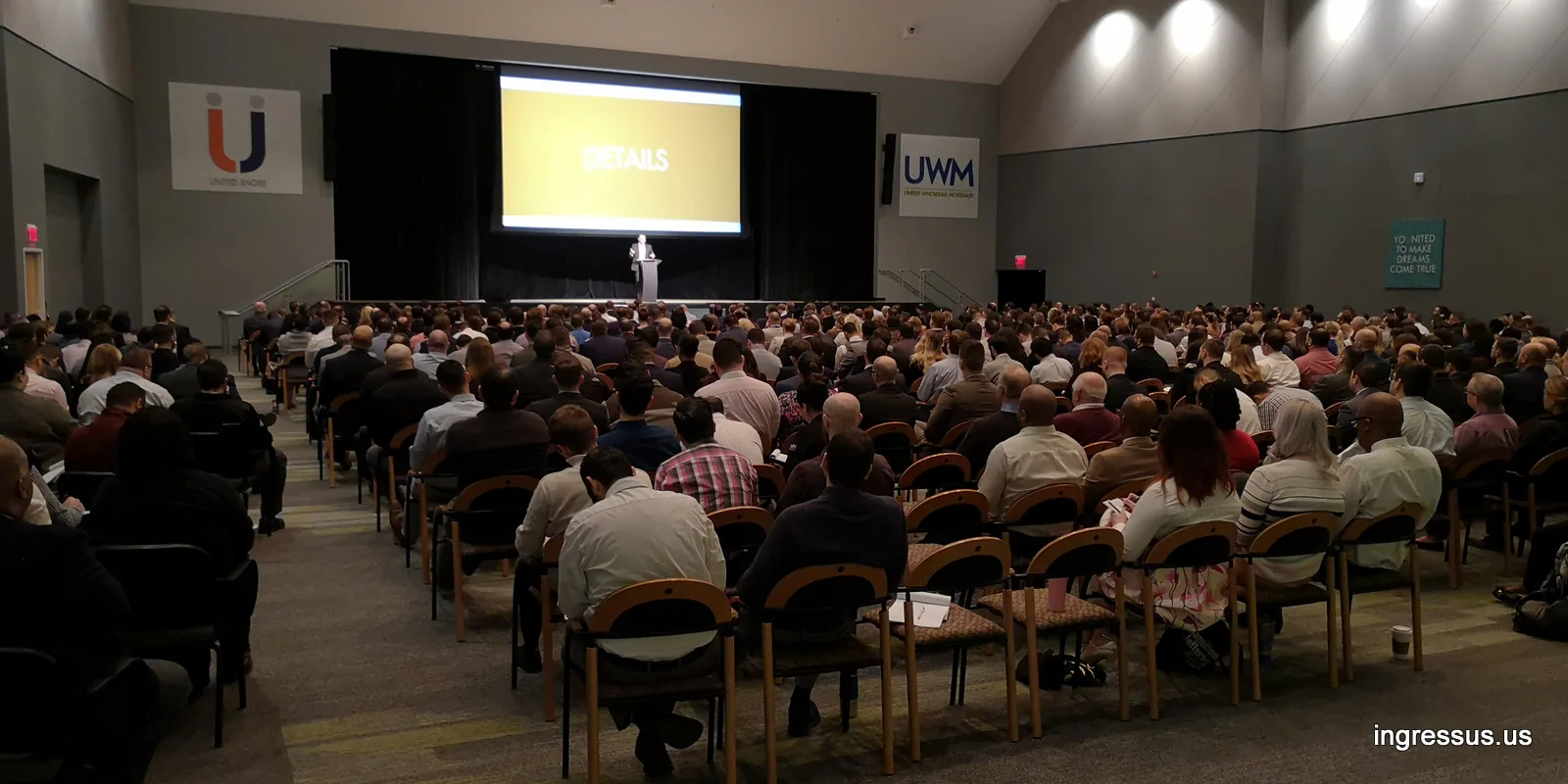 Full auditorium during Success Track sales training at United Wholesale Mortgage, with a speaker on stage and UWM signs